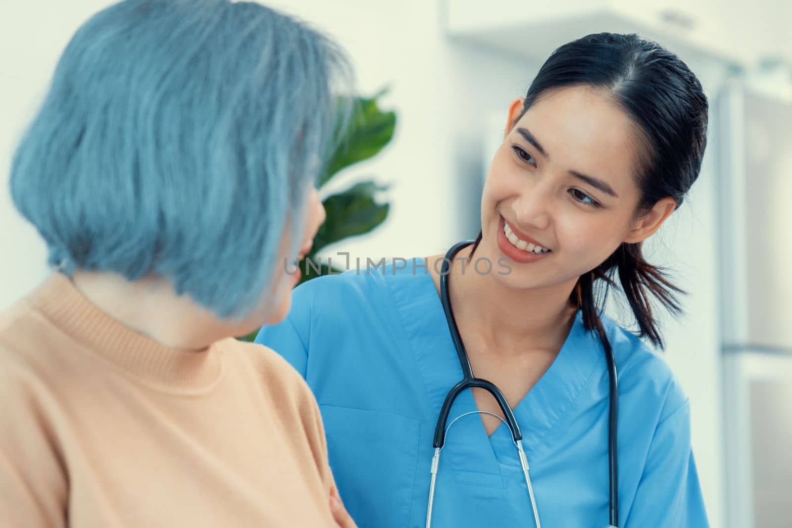 A caregiver rest her hands on the shoulders of a contented senior patient while she sitting on the sofa at home.