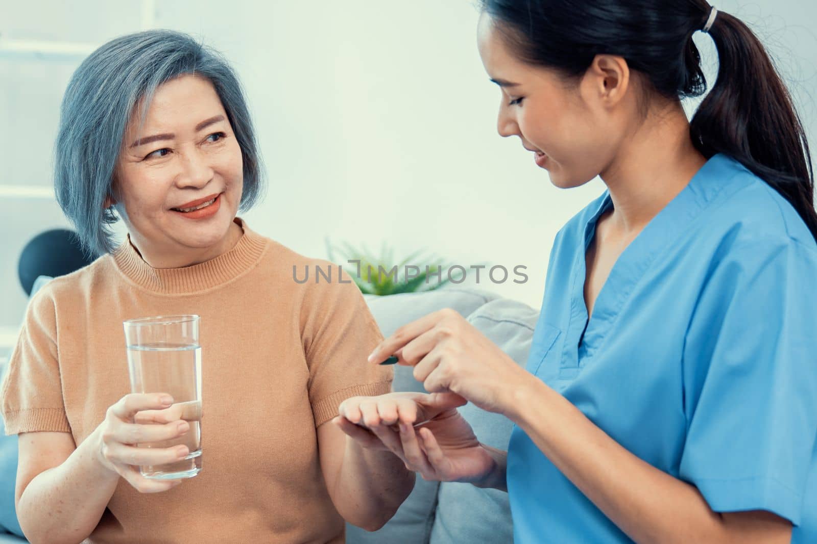 Contented senior woman taking medicines while her caregiver advising her medication. Medication for seniors, nursing house, healthcare at home.