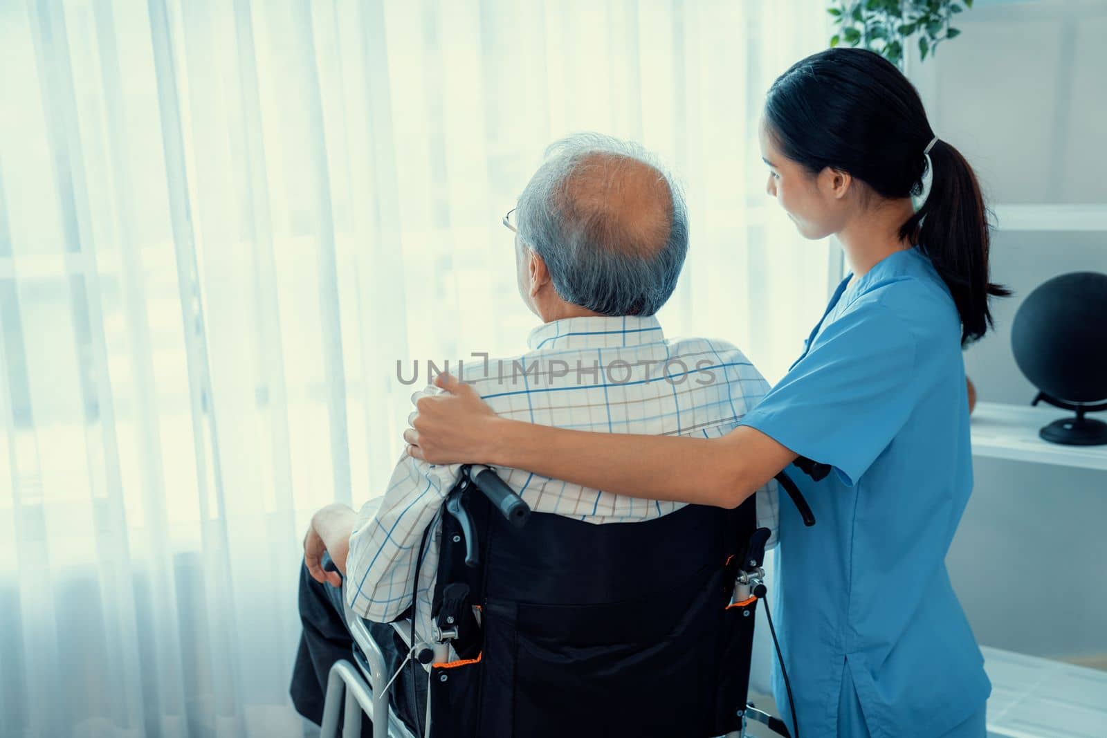 Rear view of a caregiver and her contented senior patient gazing out through the window. Elderly illness, nursing homes for the elderly, and pensioner life