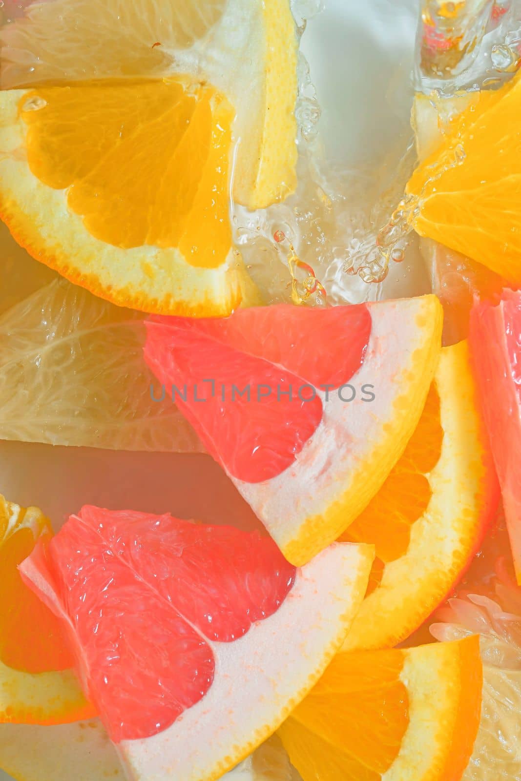 Fresh slices of grapefruit, orange fruit and honey pomelo on white background. Pieces of grapefruit, orange fruit and honey pomelo in sparkling water on white background, close-up. Vertical macro image. Top view, flat design. Summer fruit background by roman_nerud