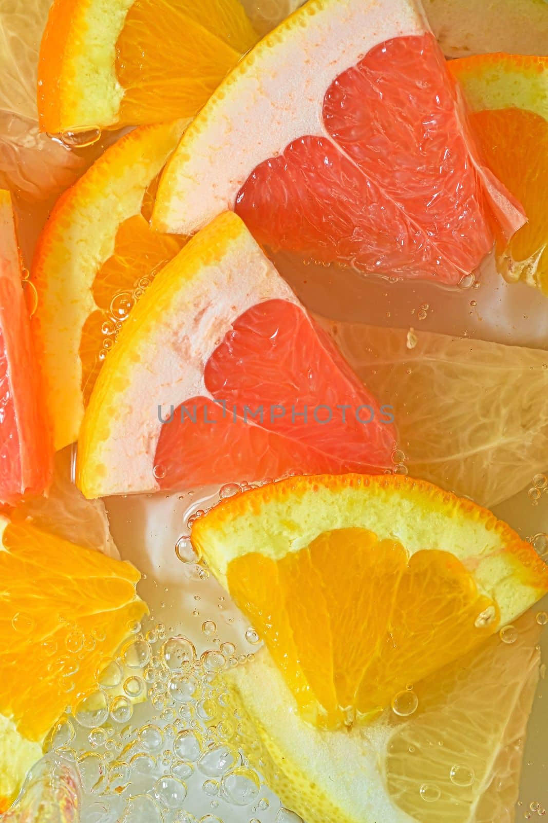 Slices of grapefruit, orange and pomelo in water on white background. Pieces of grapefruit, orange fruit and honey pomelo in liquid with bubbles. Slices of grapefruit, orange fruit and honey pomelo in water. Macro image of fruit in water. Vertical image. Top view, flat design by roman_nerud