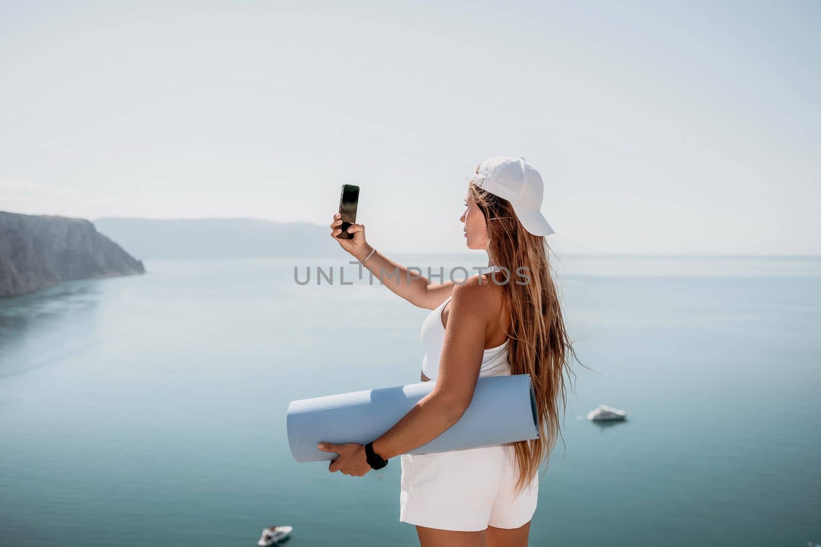 Young woman with black hair, fitness instructor in pink sports leggings and tops, doing pilates on yoga mat with magic pilates ring by the sea on the beach. Female fitness daily yoga concept