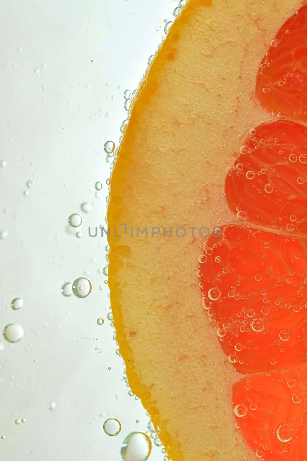 Close-up of juicy grapefruit slice on white background. Slice of red grapefruit in sparkling water on white background, close-up. Vertical macro image by roman_nerud