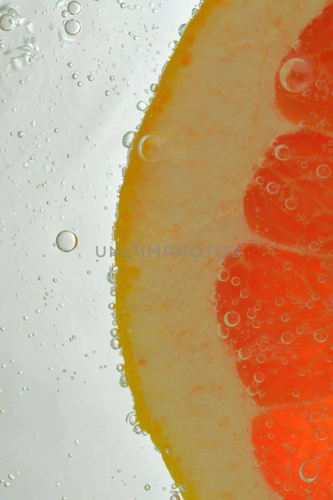 Close-up of juicy grapefruit slice on white background. Slice of red grapefruit in sparkling water on white background, close-up. Vertical macro image.