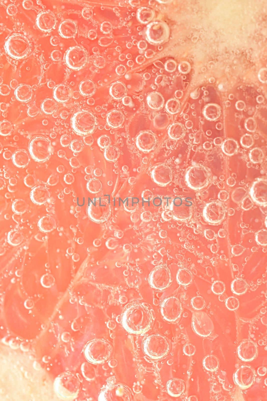 Close-up of a grapefruit slice in liquid with bubbles. Slice of red ripe grapefruit in water. Close-up of fresh grapefruit slice covered by bubbles.