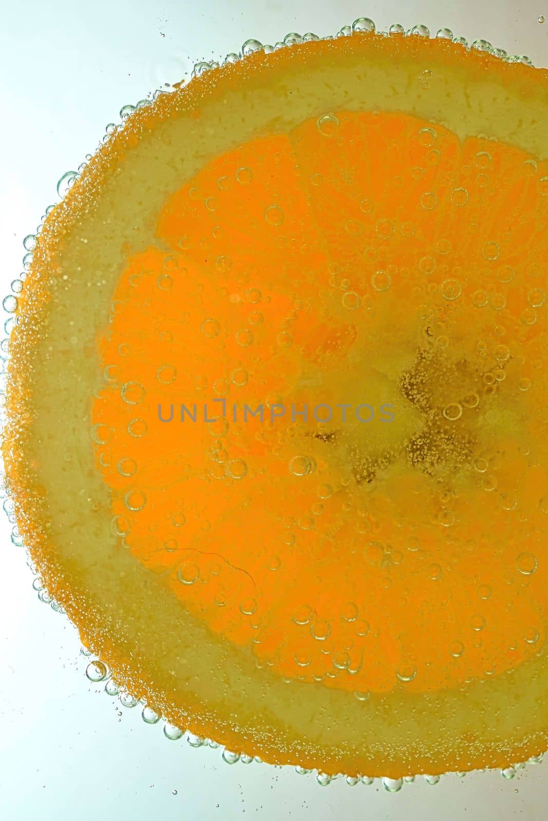 Close-up view of the orange fruit slice in water background. Texture of cooling fruit drink with macro bubbles on the glass wall. Flat design. Vertical image.