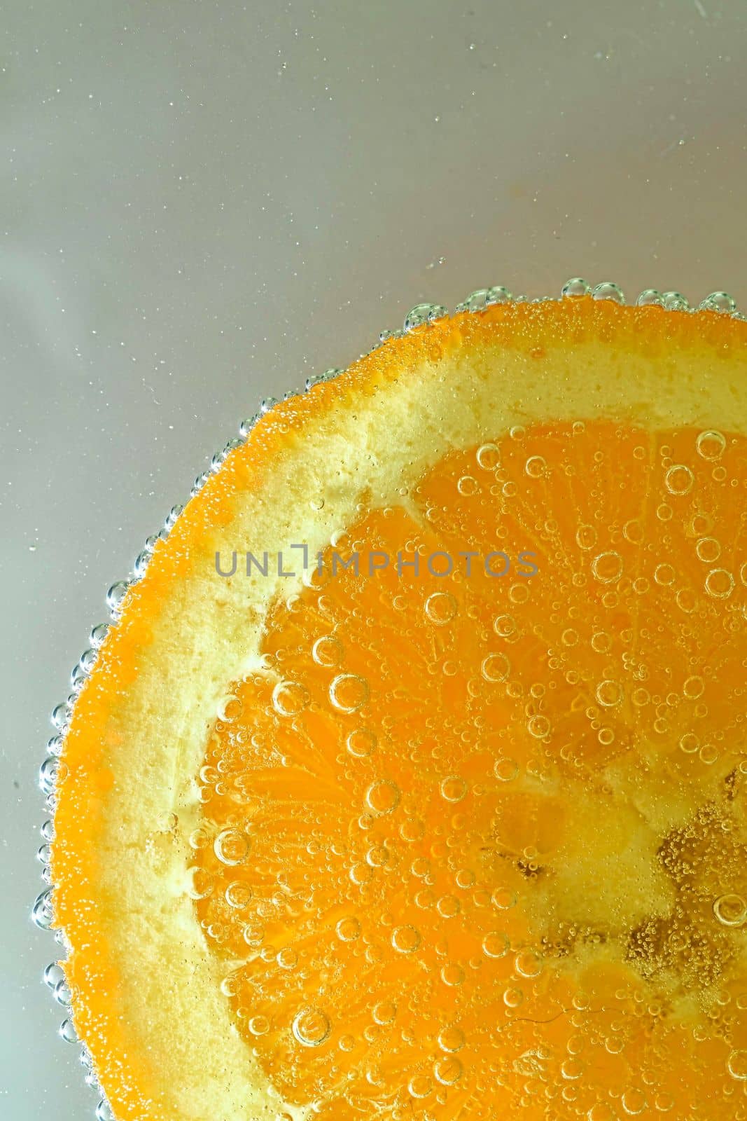 Close-up view of the orange fruit slice in water background. Texture of cooling fruit drink with macro bubbles on the glass wall. Flat design. Vertical image.