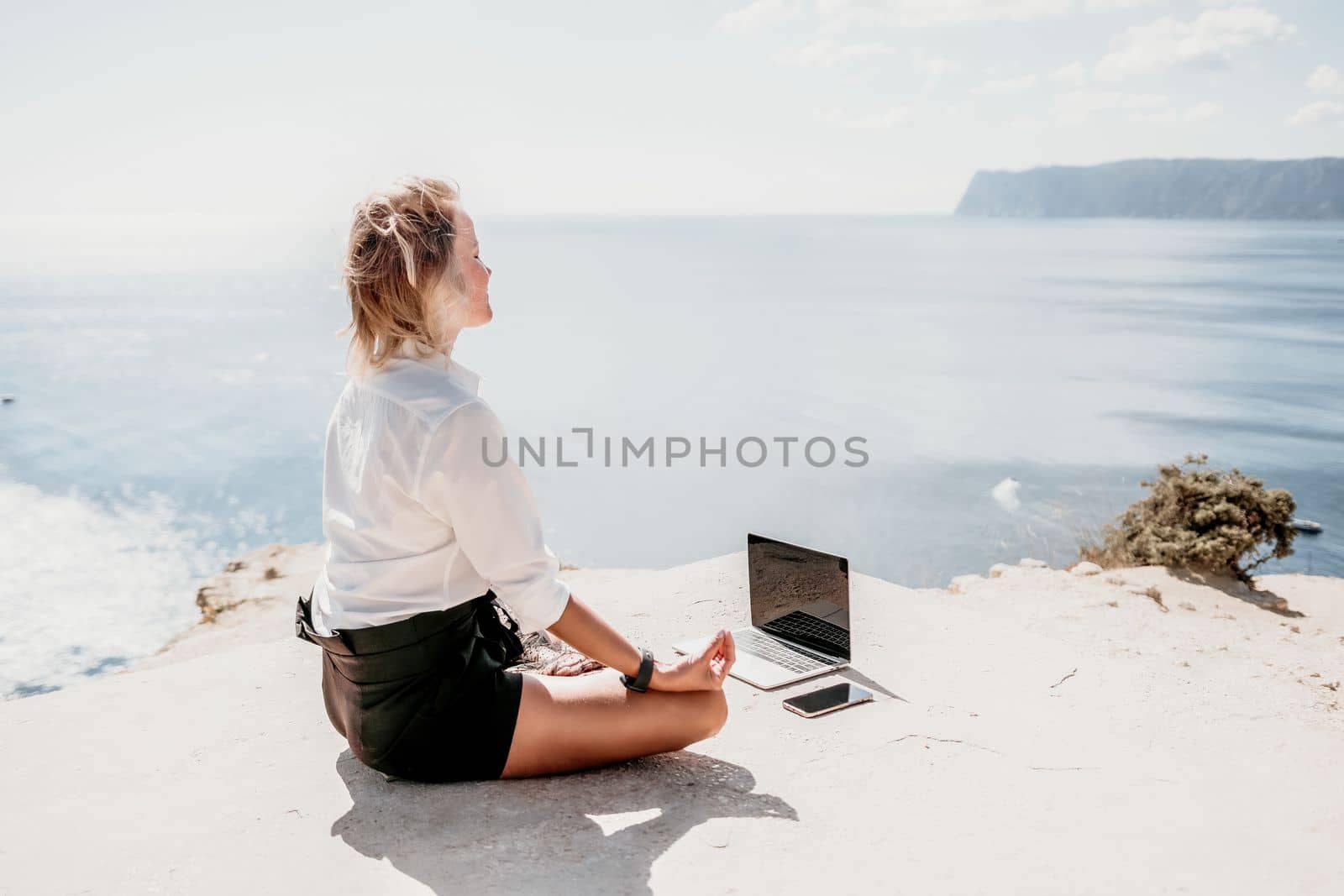Happy girl doing yoga with laptop working at the beach. beautiful and calm business woman sitting with a laptop in a summer cafe in the lotus position meditating and relaxing. freelance girl remote work beach paradise