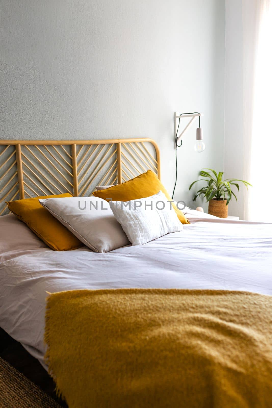 Vertical image of boho, cozy bedroom with double bed, lamps, cushions and plant. No people. by Hoverstock