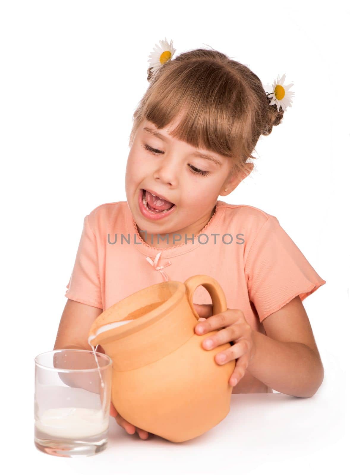 Healthy food. A little girl in an orange T-shirt and flowers in her hair pours fresh milk from a jug on a white background