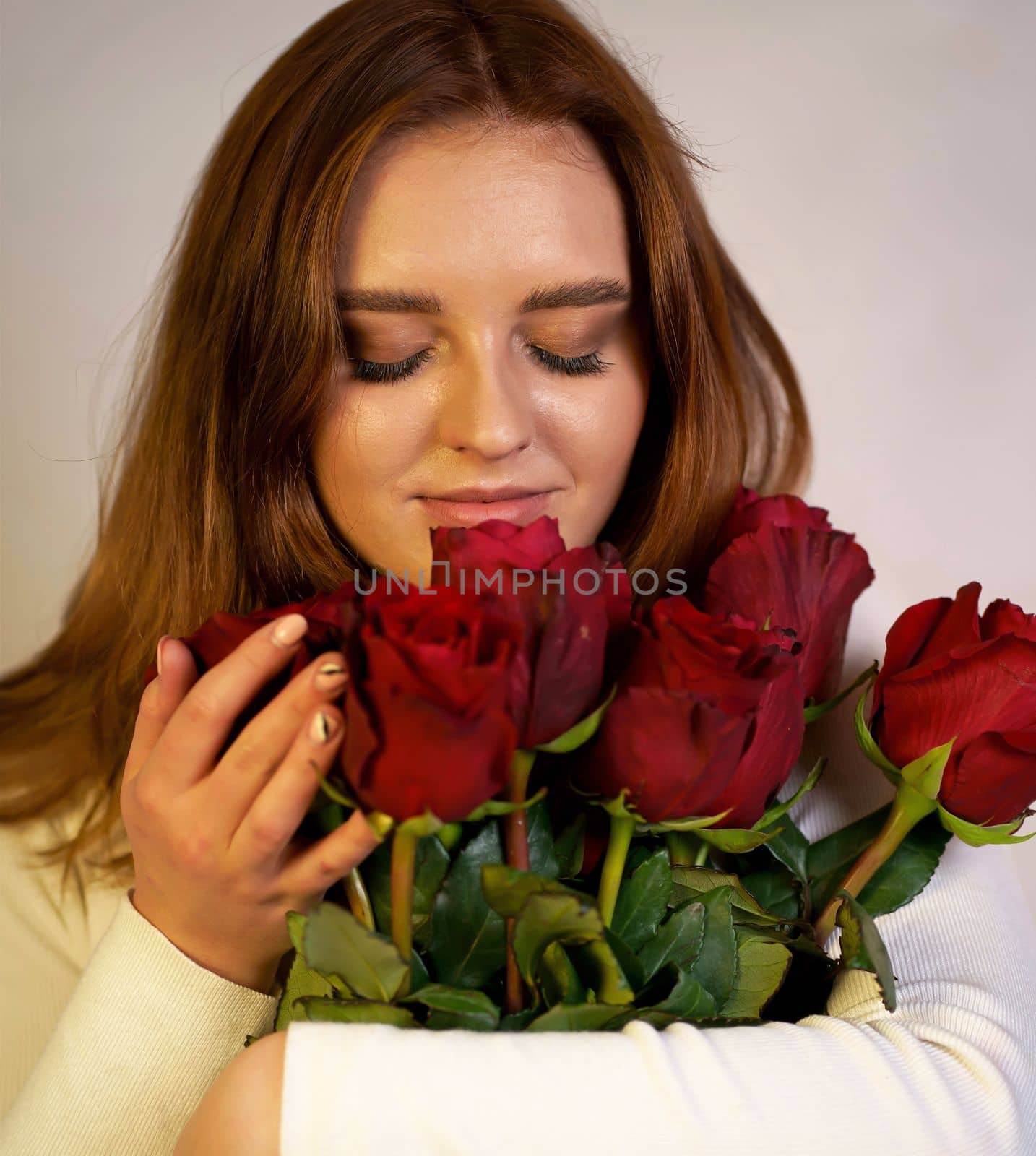 Portrait of a young woman in a white blouse holding a bouquet of roses on a pink background. Valentine's Day by aprilphoto