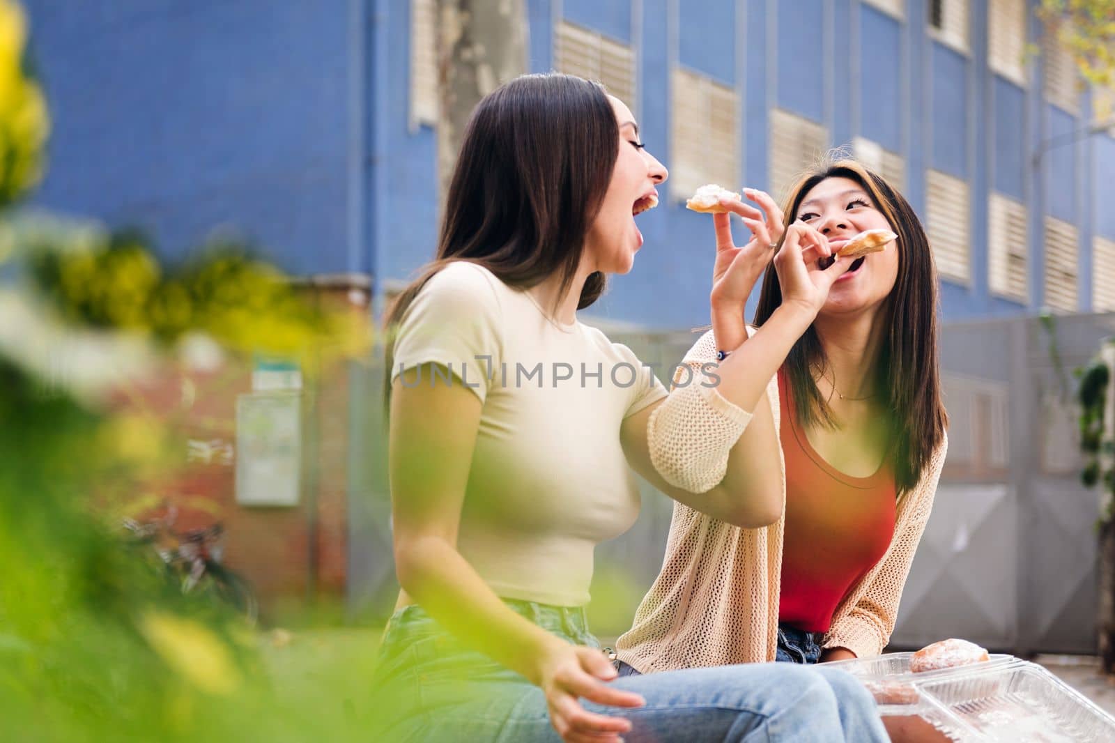 couple of young women sharing some sweet buns sitting in a city park, concept of friendship and love between people of the same sex