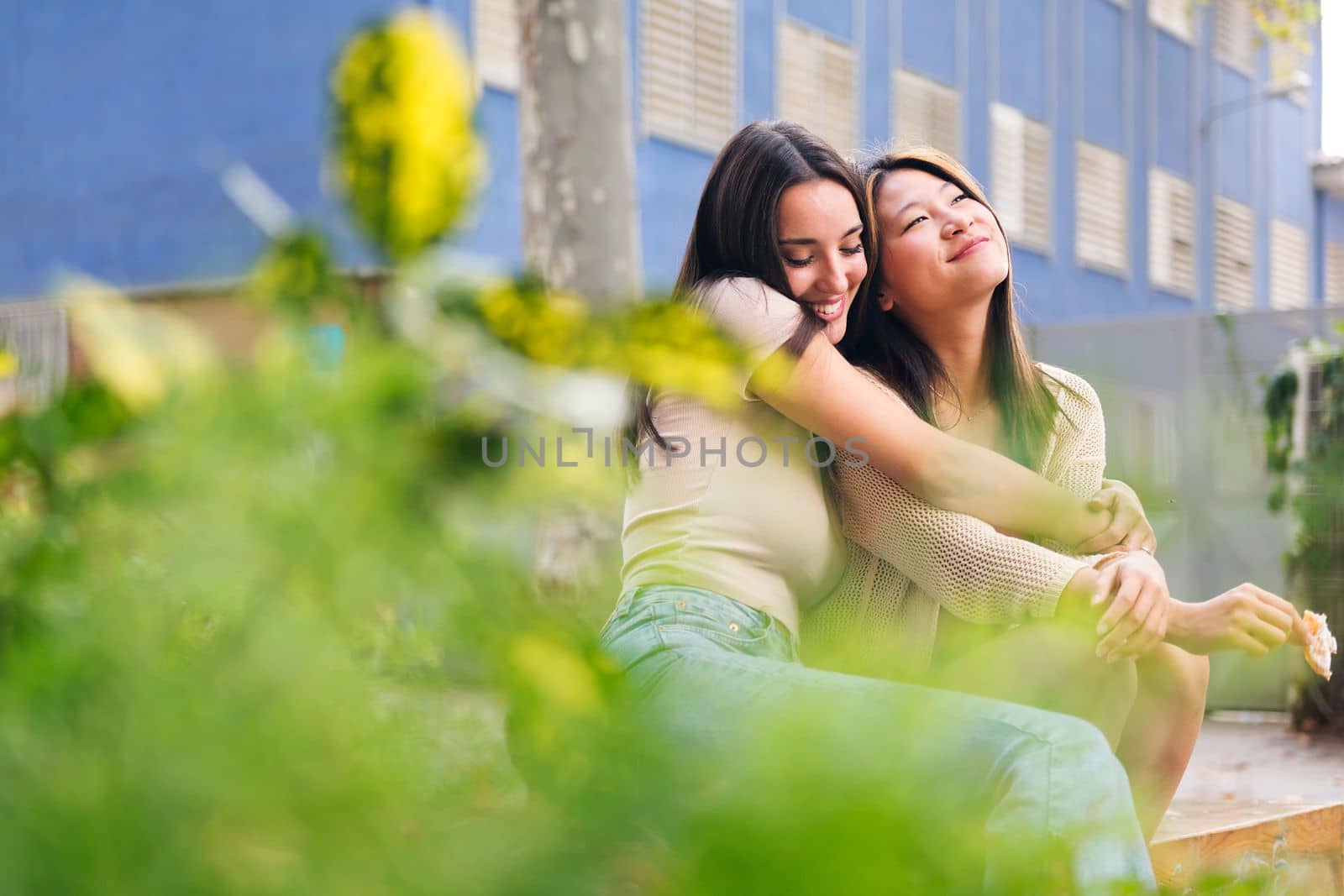 couple of young women embracing each other sitting in a city park, concept of friendship and love between people of the same sex