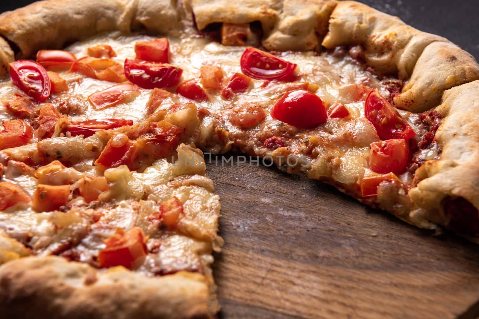close up of tasty sliced pizza with tomatoes and herbs without one slice over wooden table background