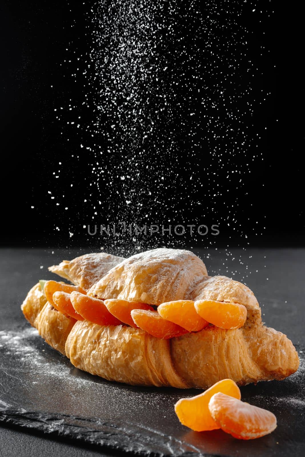 Sweet croissant sandwich with powdered sugar on a dark background. Baking and bakery concept.
