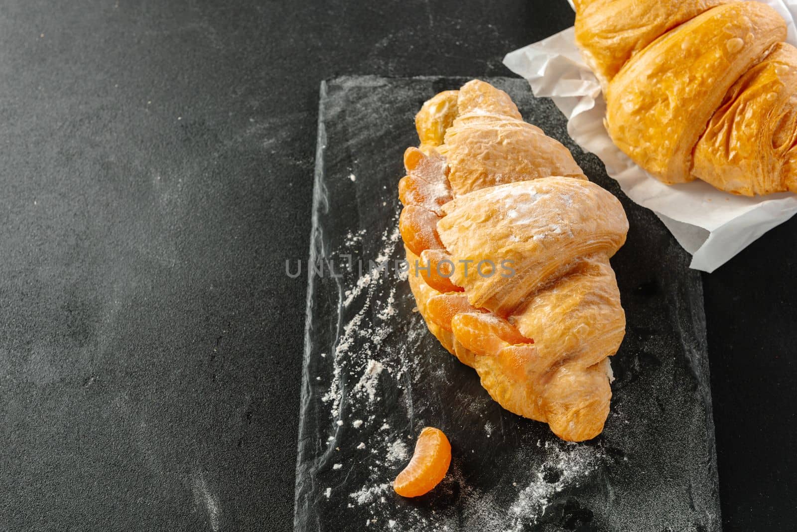 Sweet croissant sandwich with tangerines on dark background. Copy space.