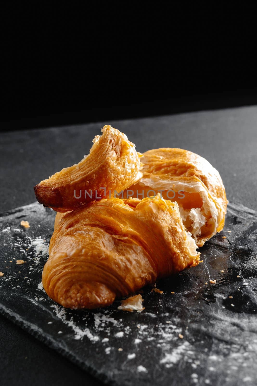 Close-up of croissants on a dark background. One croissant broken into pieces by gulyaevstudio