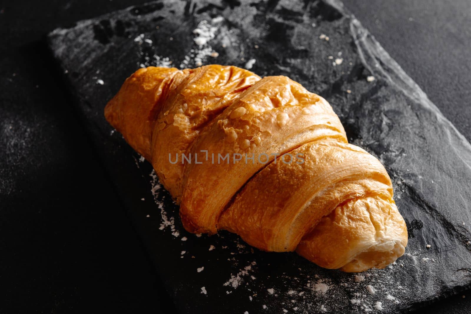 Large croissant on black background. Fresh and delicious French pastries, bakery concept, close-up image by gulyaevstudio