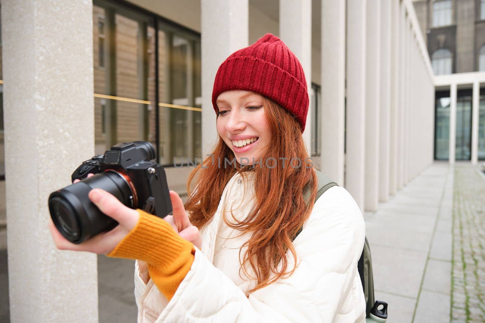 Beautiful readhead girl, photographer with professional camera takes pictures outdoors, walking around city and taking photos, sightseeing.