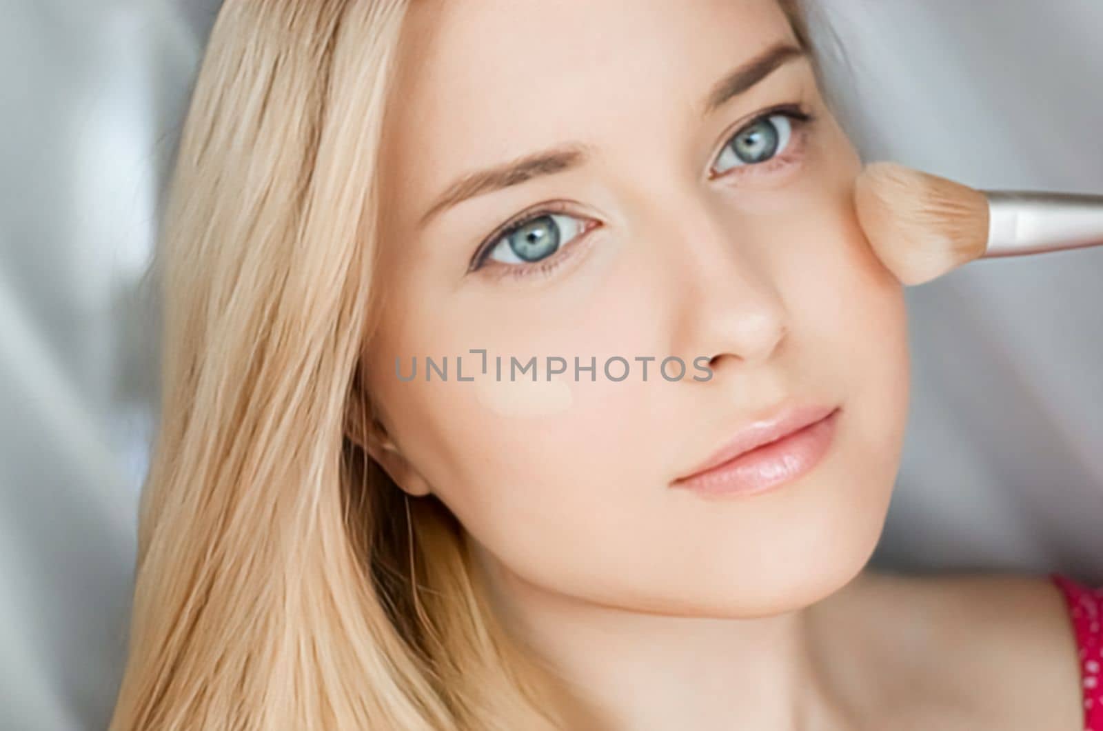 Beautiful blonde woman applying liquid make-up foundation on her skin with make-up brush.