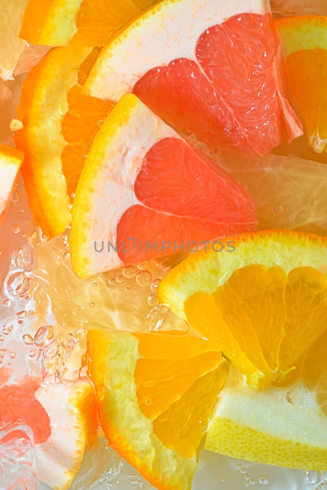 Slices of grapefruit, orange and pomelo in water on white background. Pieces of grapefruit, orange fruit and honey pomelo in liquid with bubbles. Slices of grapefruit, orange fruit and honey pomelo in water. Macro image of fruit in water. Vertical image. Top view, flat design by roman_nerud