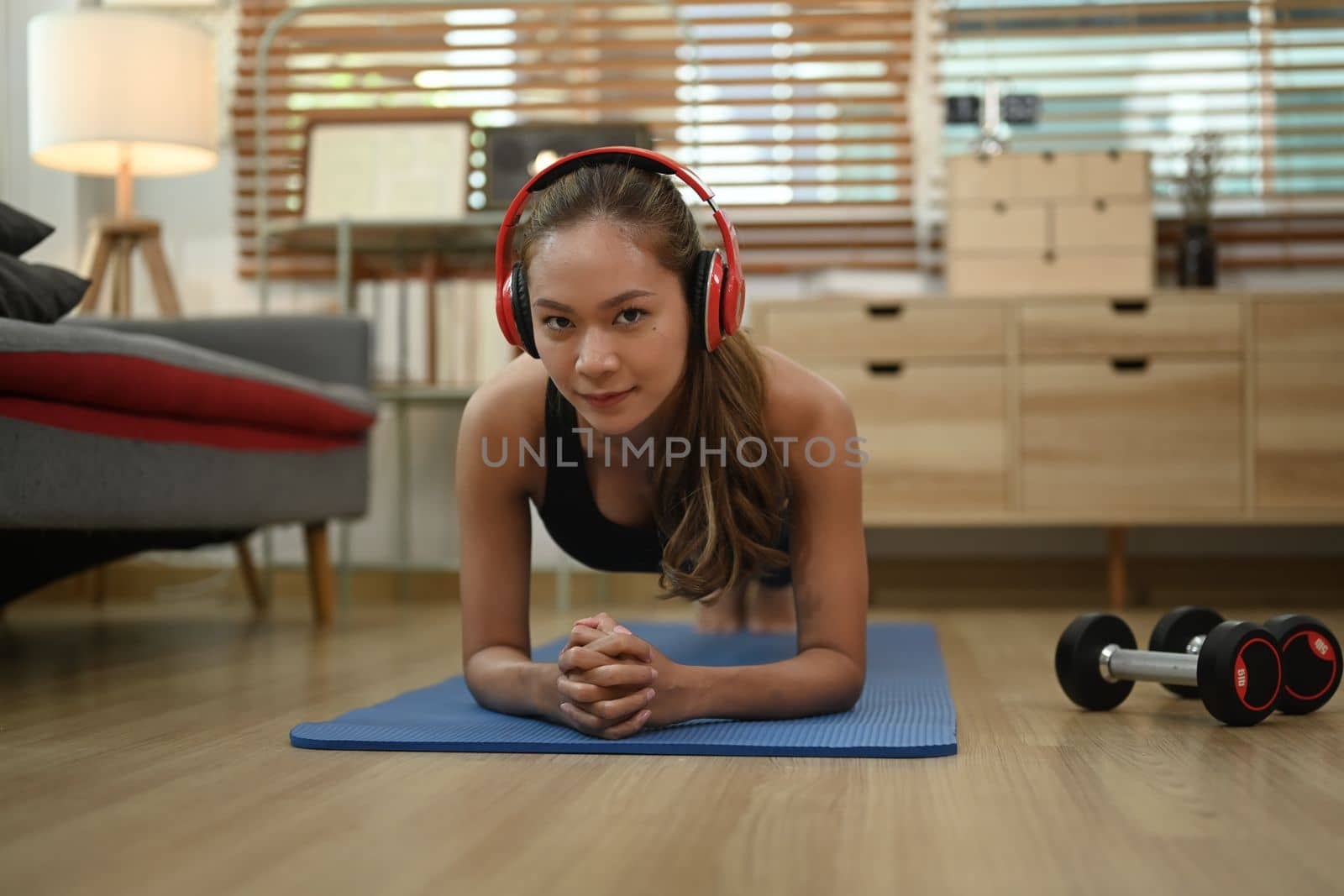 Strong athletic woman with wireless headphone doing plank exercise on matin living room by prathanchorruangsak