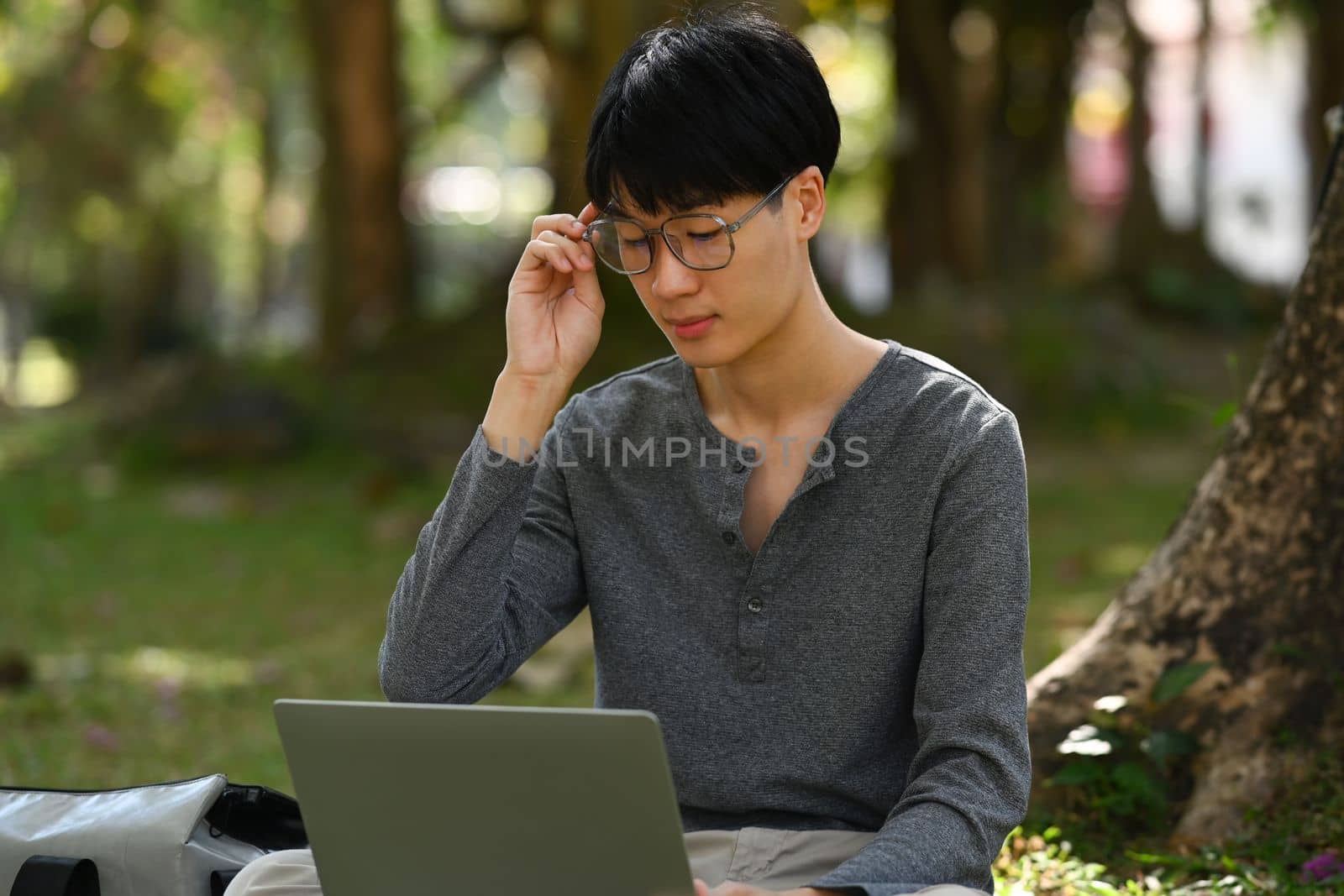 Smart asian student man doing homework, using laptop against calm nature park in sunny day. Technology and education concept.