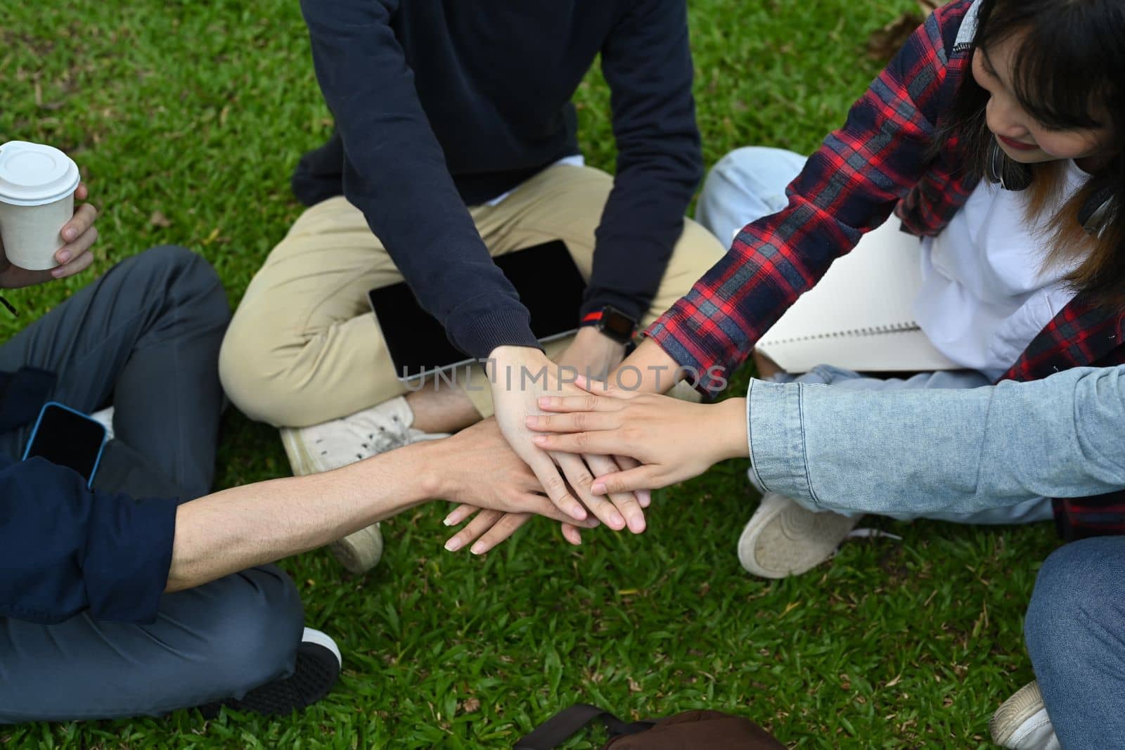 Above view of university friends stacking hands together, showing unity and togetherness. Youth lifestyle and friendship concept.