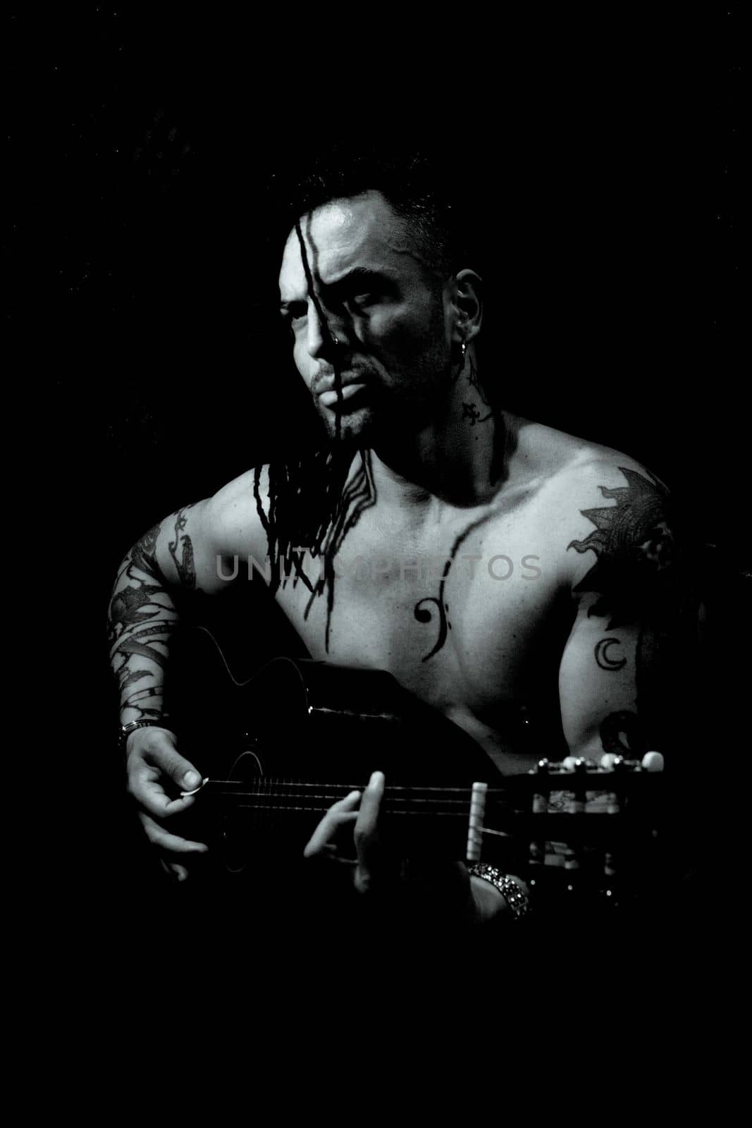 Man playing guitar and singing shirtless. Dark background