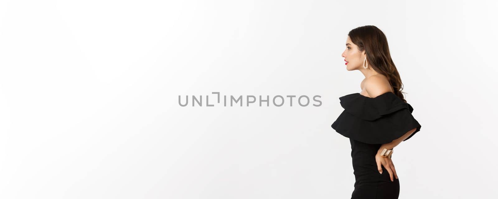 Profile view of beautiful woman in elegant black dress, standing over white background. Copy space