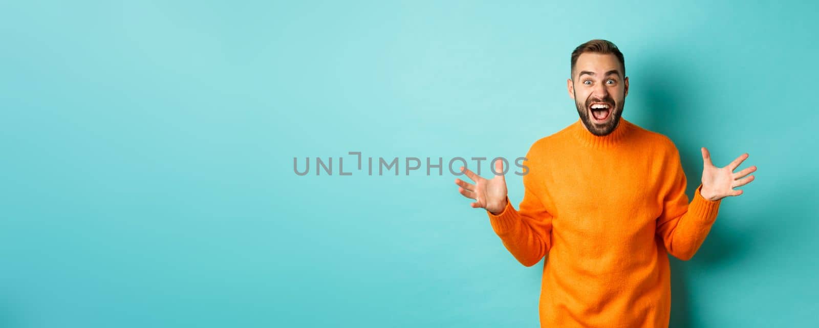 Image of happy and excited man announce big news, spread hands and shouting of joy, rejoicing, standing over light blue background by Benzoix