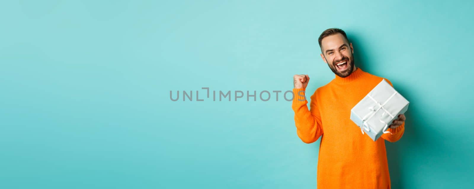 Holidays and celebration concept. Excited man receiving gift, looking happy at present and smiling, standing over blue background by Benzoix