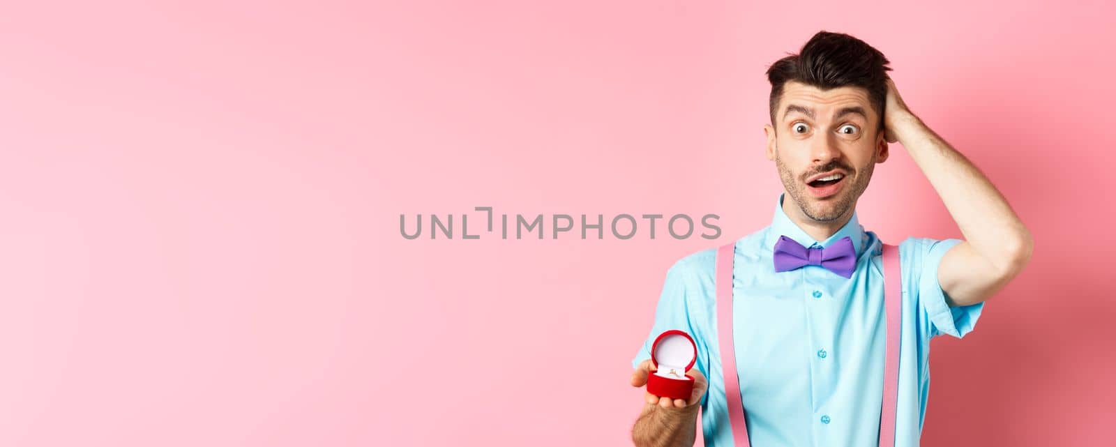Valentines day. Confused funny guy standing with engagement ring, scratching head with unsure face, dont know what say, making proposal, standing over pink background by Benzoix