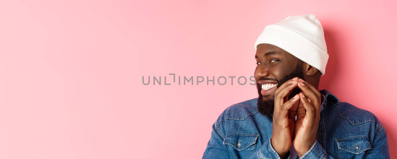 Close-up of devious african-american male model having an idea, scheming something, steeple fingers and smiling sly, standing over pink background by Benzoix