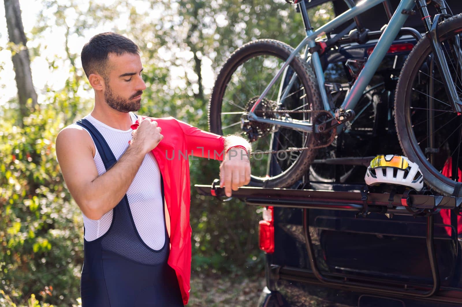 young man dressing up with cycling clothes next to his van to go training with his mountain bike, concept of freedom and sport in nature