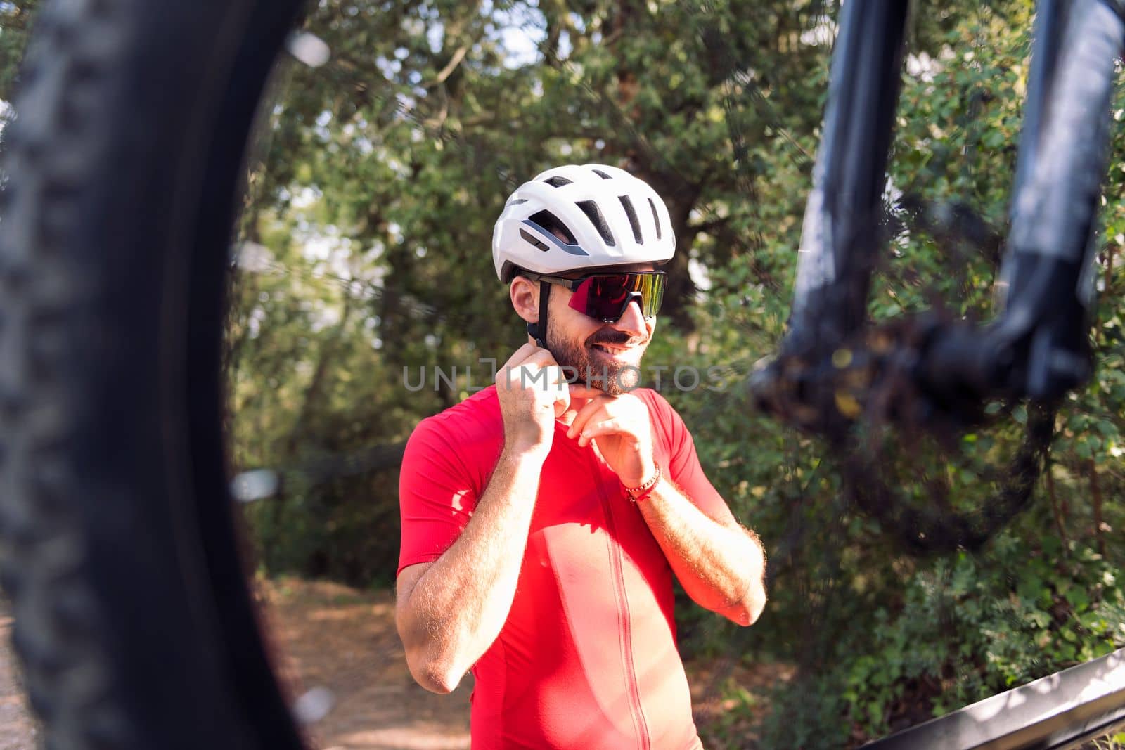 smiling young man putting on cycling helmet next to his van to go training with his mountain bike, concept of freedom and sport in nature