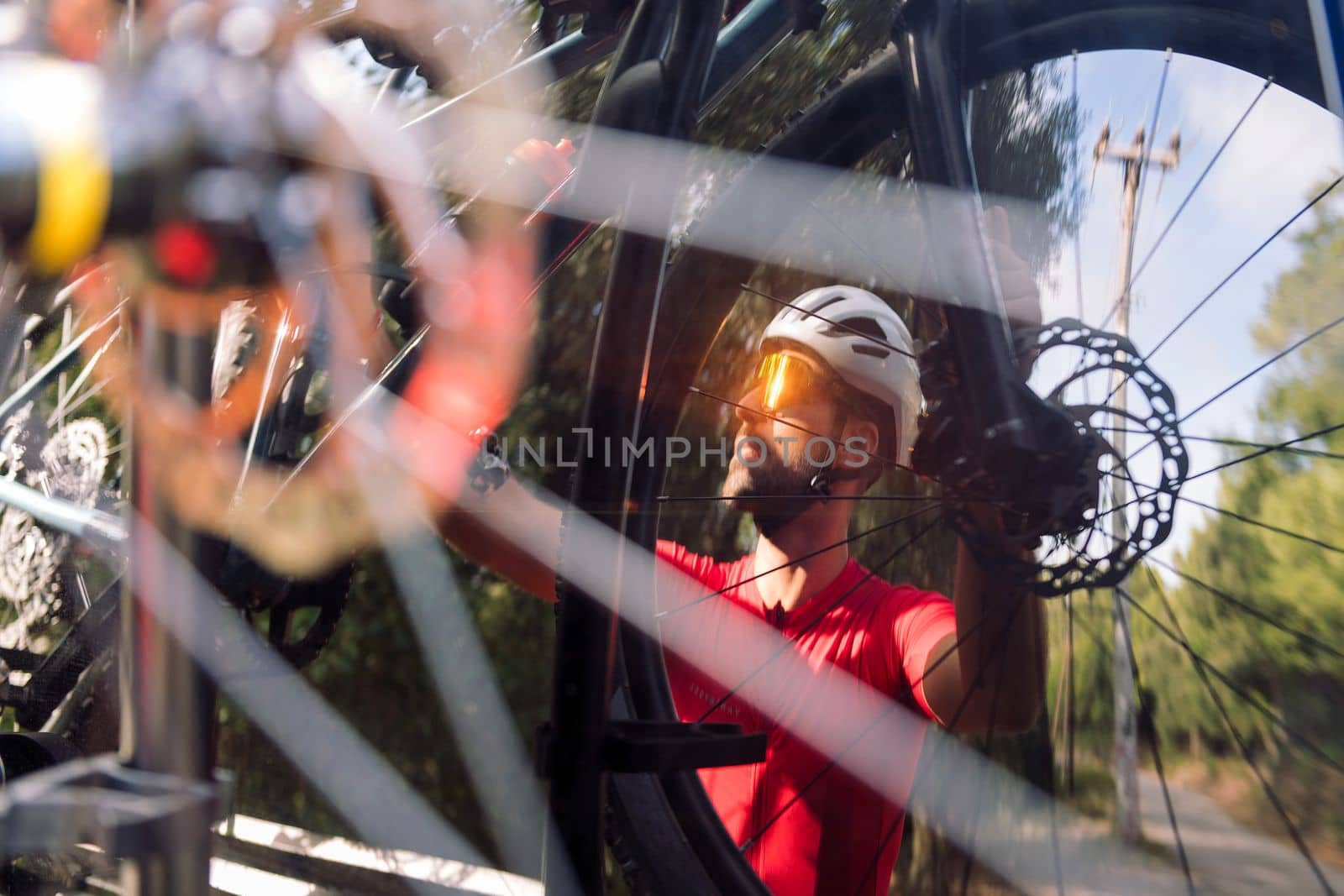 reflection in the rear window of a van of a young man wearing a helmet and cycling goggles taking his mountain bike off the bike rack for a training ride, concept of freedom and sport in nature