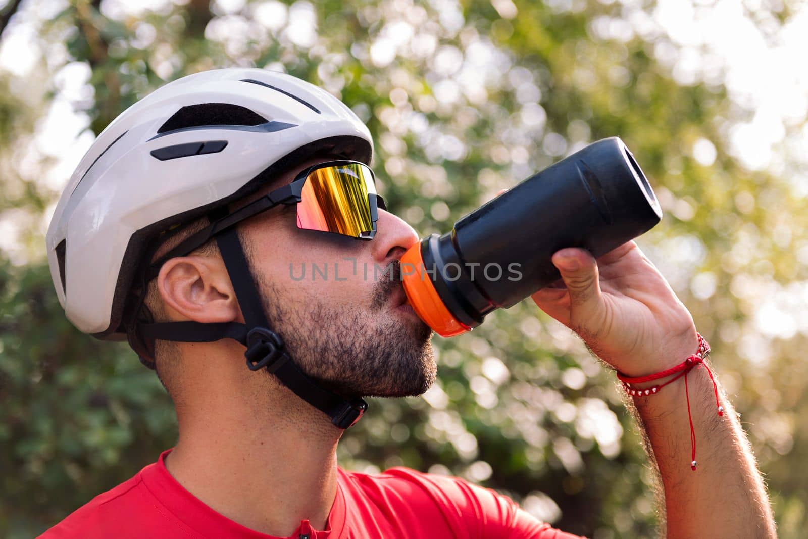 young man wearing a helmet and cycling goggles drinking water from his bottle, concept of freedom and sport in nature
