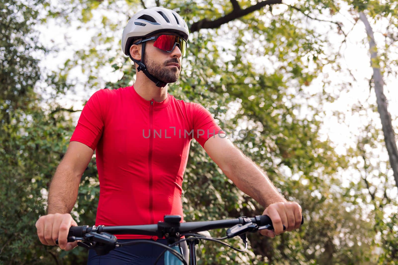 portrait of a young man in cycling clothes with his mountain bike in the middle of the forest, concept of freedom and sport in nature, copy space for text