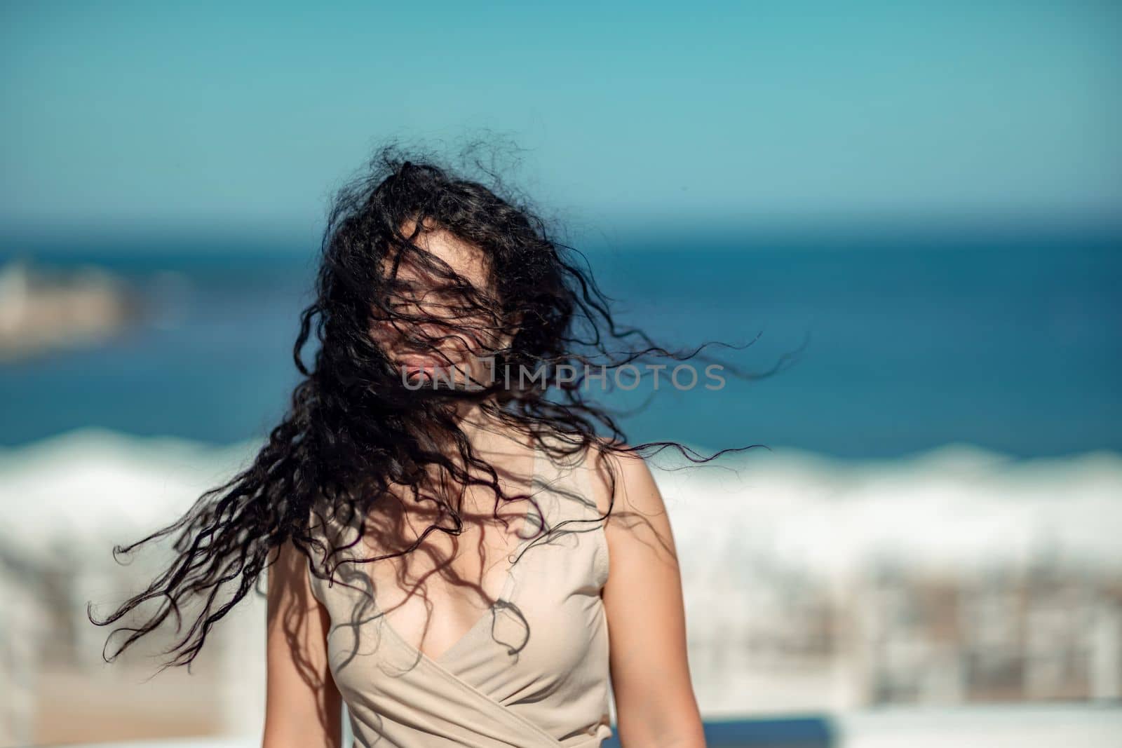 Sea woman rest. Portrait of a woman with long curly black hair in a beige dress stands on a balcony against the backdrop of the sea. Tourist trip to the sea