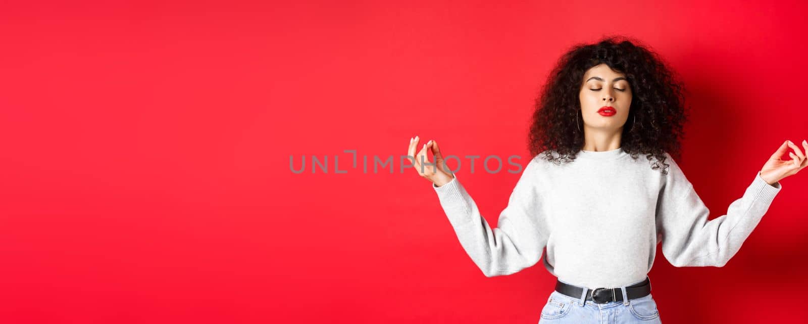 Woman in casual clothes trying to calm down with meditation, close eyes and practice yoga, holding hands sideways with zen gesture, standing on red background by Benzoix