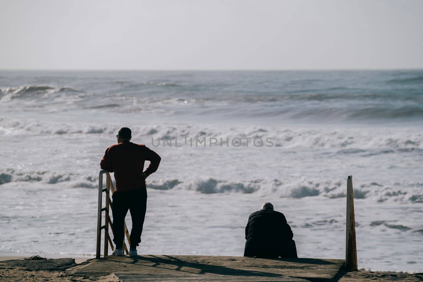 Silhouette of two adults looking at wild sea waves in calm and relaxed state by papatonic