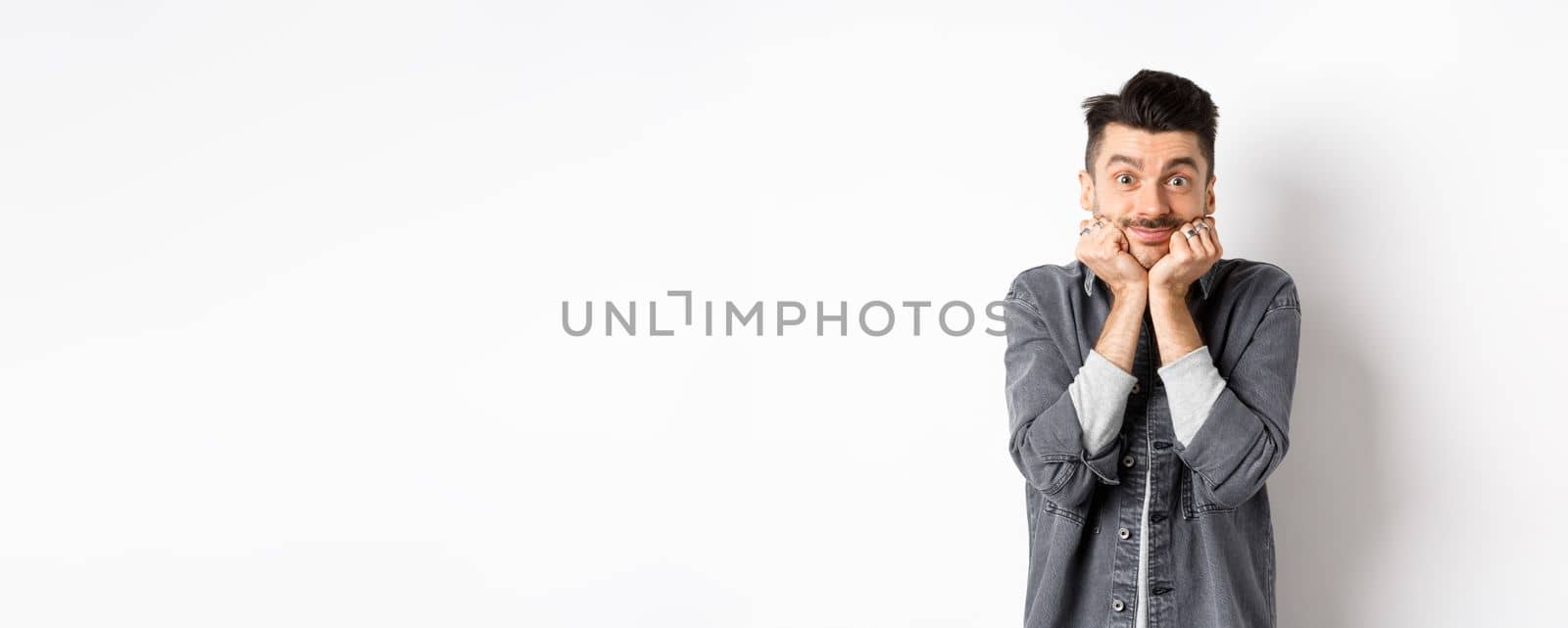 Cute young man with moustache smiling and looking dreamy at camera, gazing at something beautiful, admire true beauty, standing on white background.