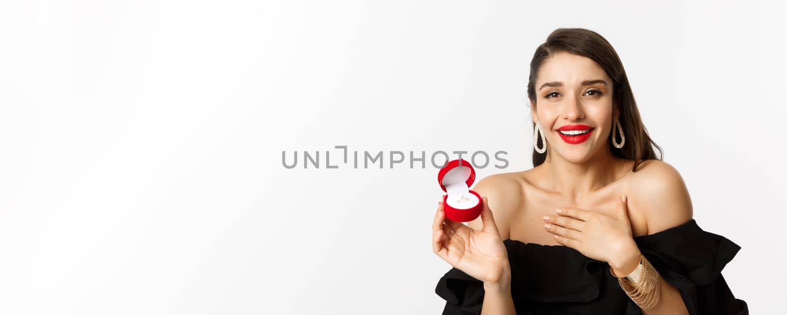 Close-up of happy woman showing her engagement ring, receive marriage proposal, saying yes, standing over white background.