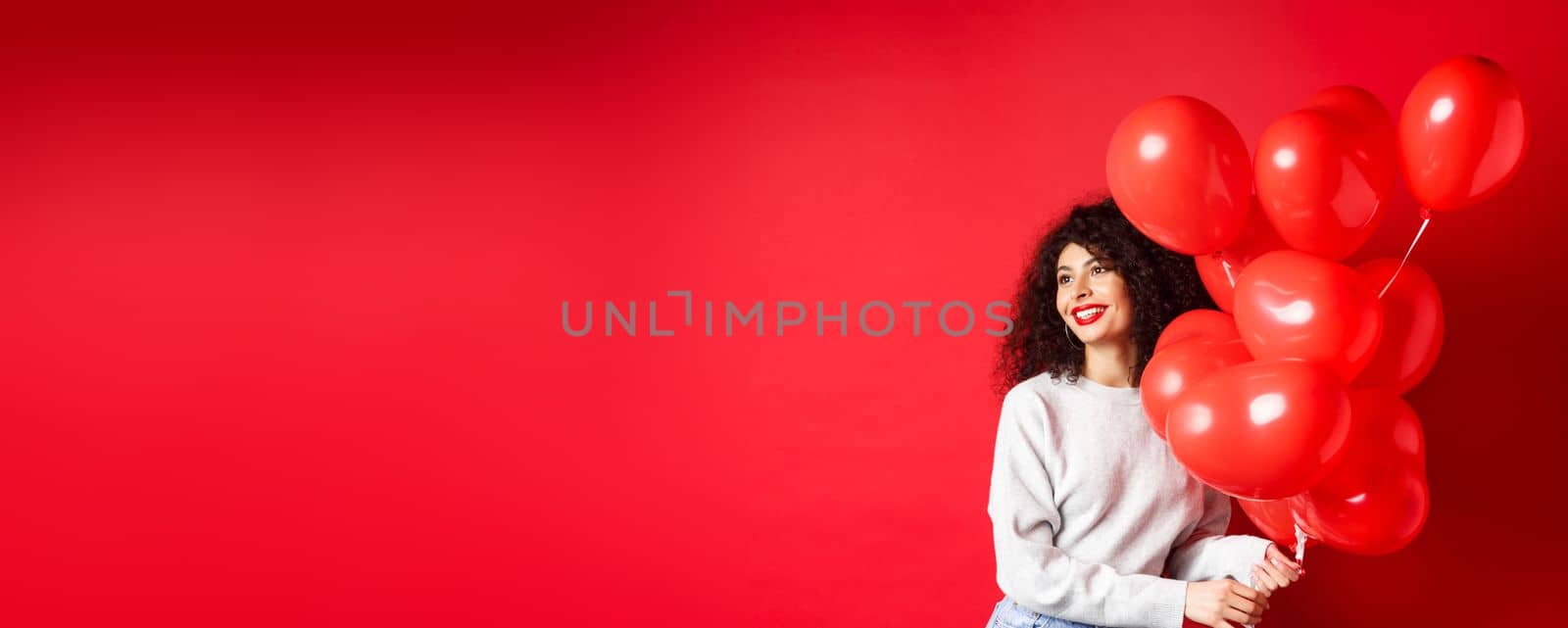 Holidays and celebration. Happy woman posing with party balloons on red background, looking aside at empty space by Benzoix