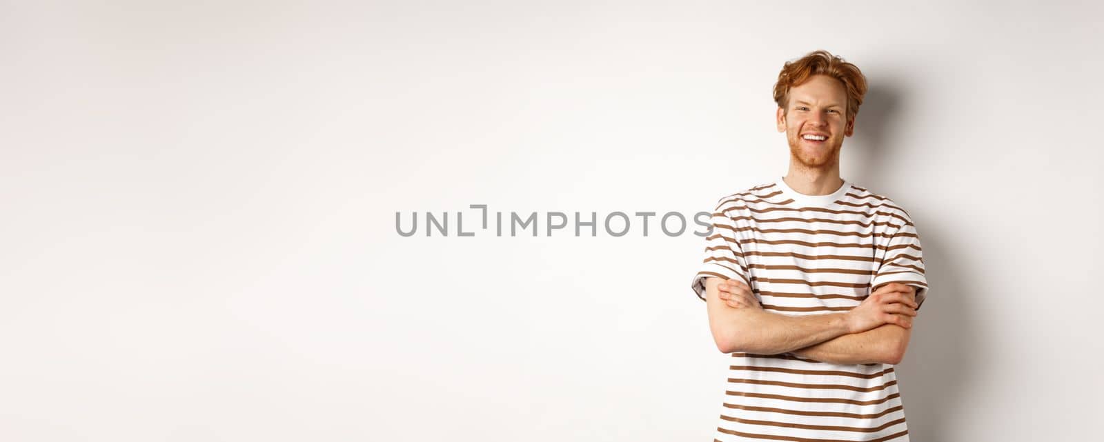 Happy redhead guy with bristle laughing and smiling at camera, standing with hands crossed on chest over white background.