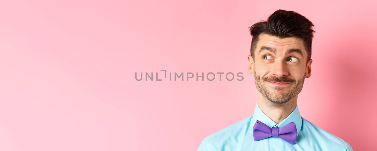 Close-up of handsome smiling guy with moustache, looking left at logo with pleased face, standing on pink background by Benzoix