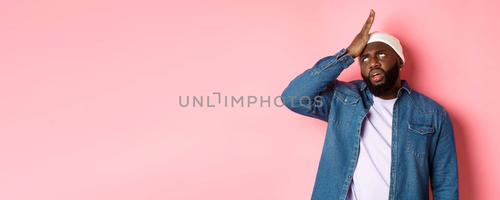 Annoyed Black man roll his eyes and facepalm, standing bothered and tired against pink background by Benzoix