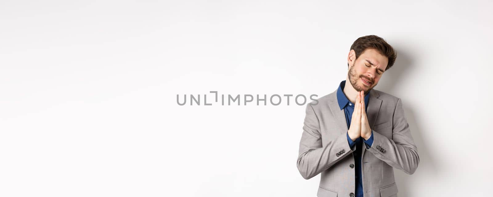 Pleading businessman begging for help, holding hands in pray and asking for favour, need something, say please, standing on white background.