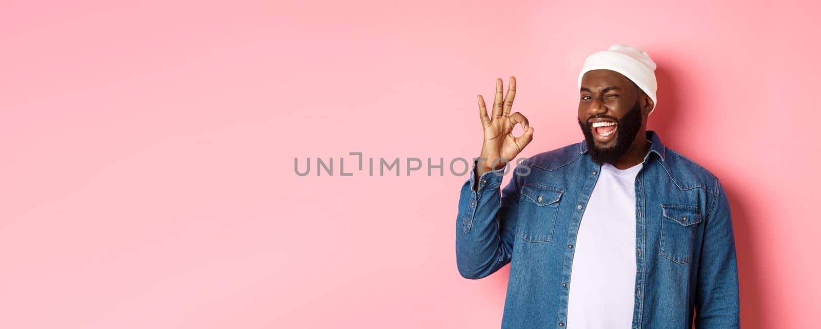 Happy smiling african american man showing okay sign, approve and praise good offer, standing over pink background by Benzoix